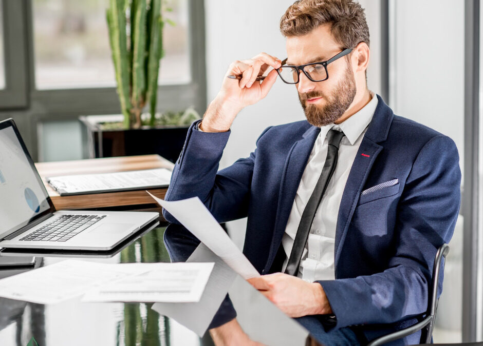 Professional man in a suit reviewing commercial loan documents in a modern office setting with a laptop.